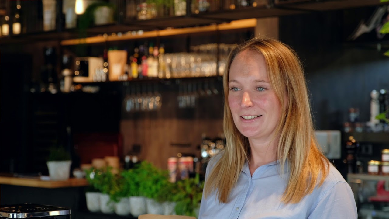 Woman in cafe smiling, blonde hair, blue shirt, bar background