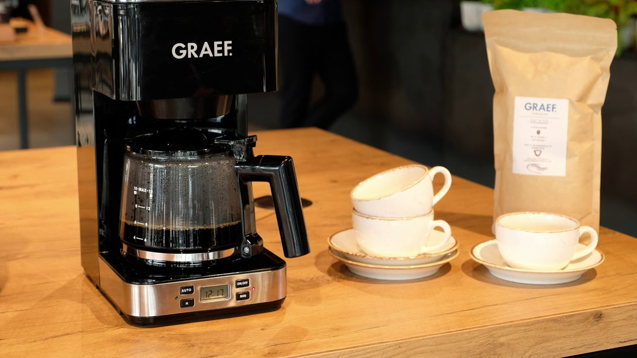 Kaffeemaschine mit Tassen und Kaffeebohnen auf einem Holztisch.