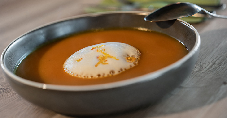 Suppe in einer Schüssel mit Schaum und Orangenschale