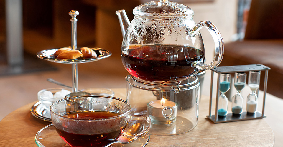 Tee-Set mit Teekanne, Tasse, Gebäck, Sanduhren und Kerze auf Holz