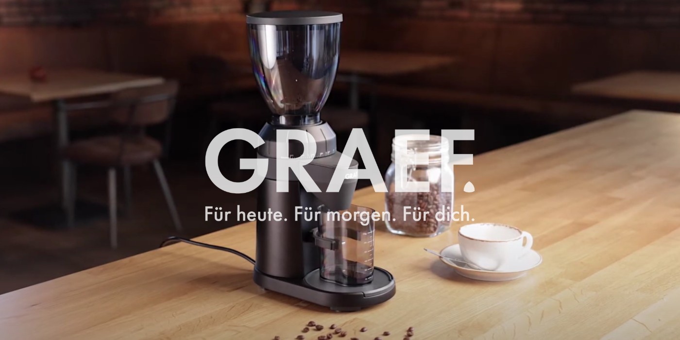 Coffee grinder with coffee beans and cup on a wooden table. GRAEF.