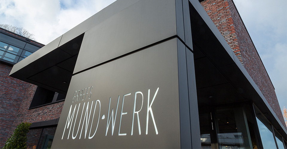 Gebäude mit Schild 'Graefs Mund-Werk' und Backsteinmauer im Hintergrund.