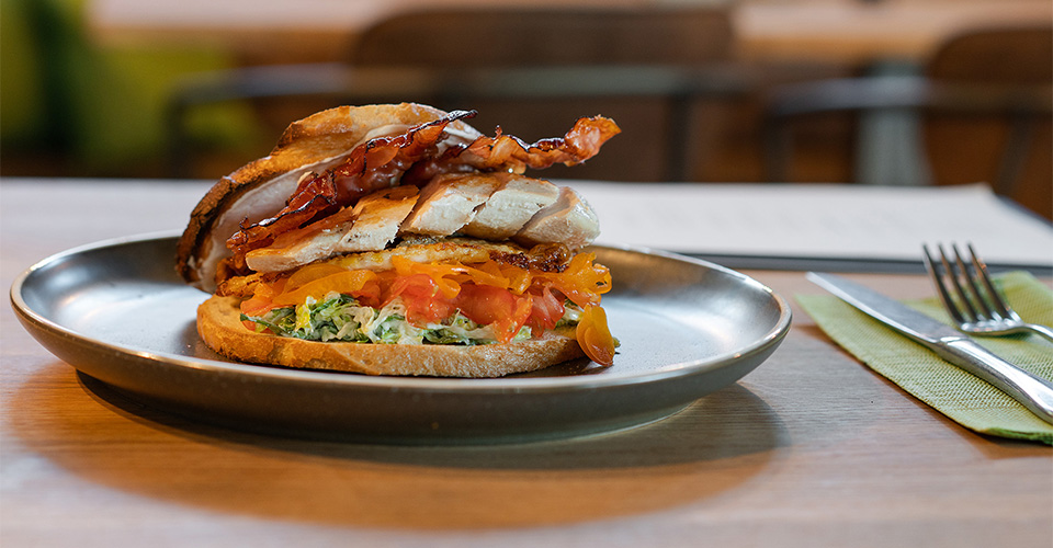 Ein Sandwich mit Hühnchen, Speck und Gemüse auf einem Teller mit Besteck.