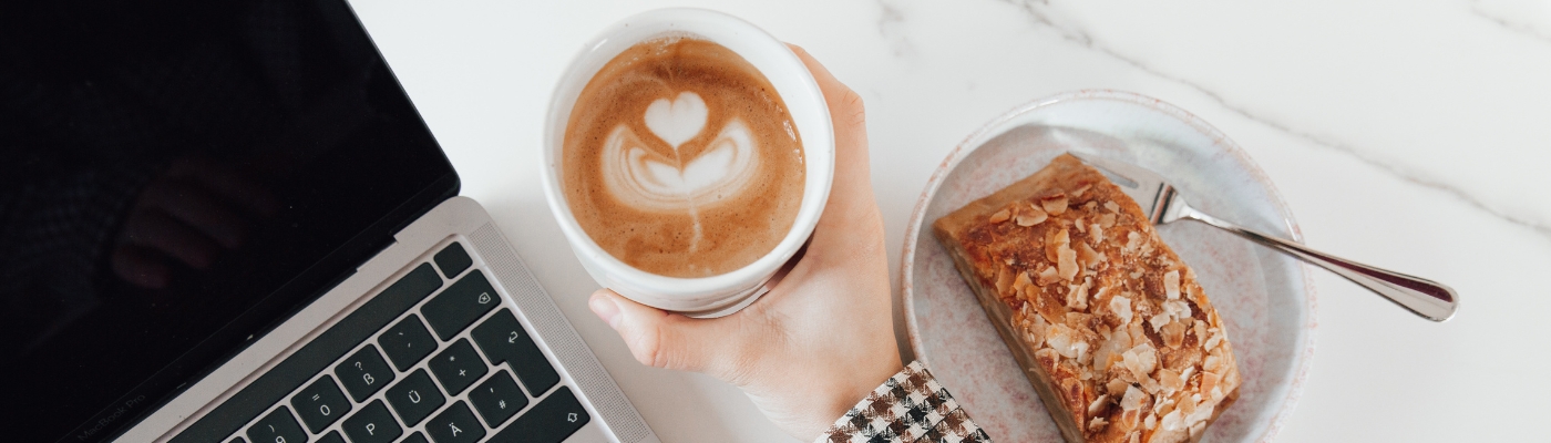 Kaffee, Kuchen und Laptop auf weißem Marmortisch. Gemütliche Pause.