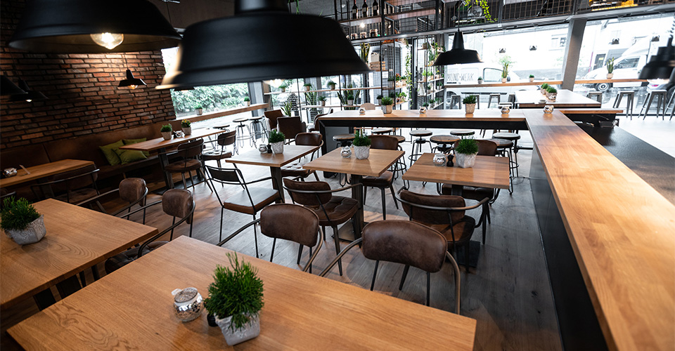 Ein gemütliches Restaurant mit Holztischen und Stühlen, Pflanzen und Lampen.