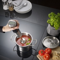 Person püriert Tomatensuppe mit einem Stabmixer in einem Topf.