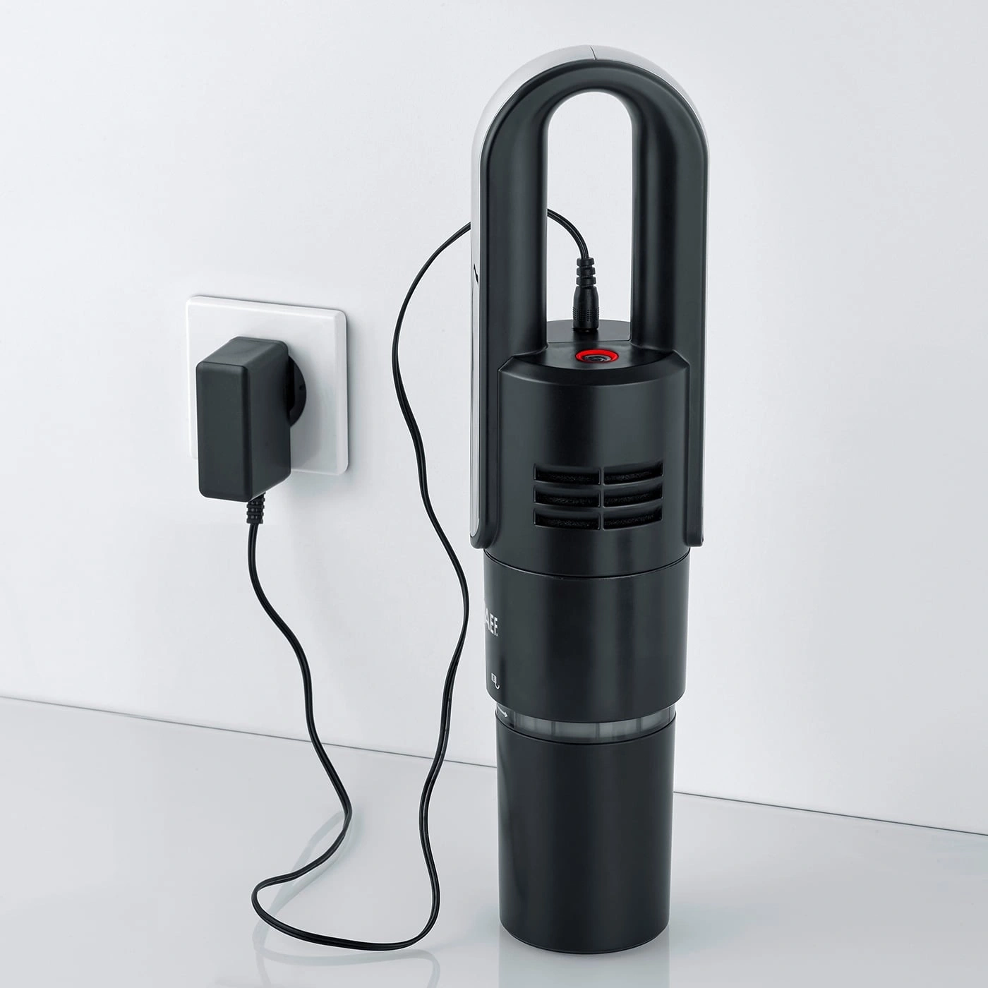 Black vacuum cleaner with charger on the wall, ready to charge and use.