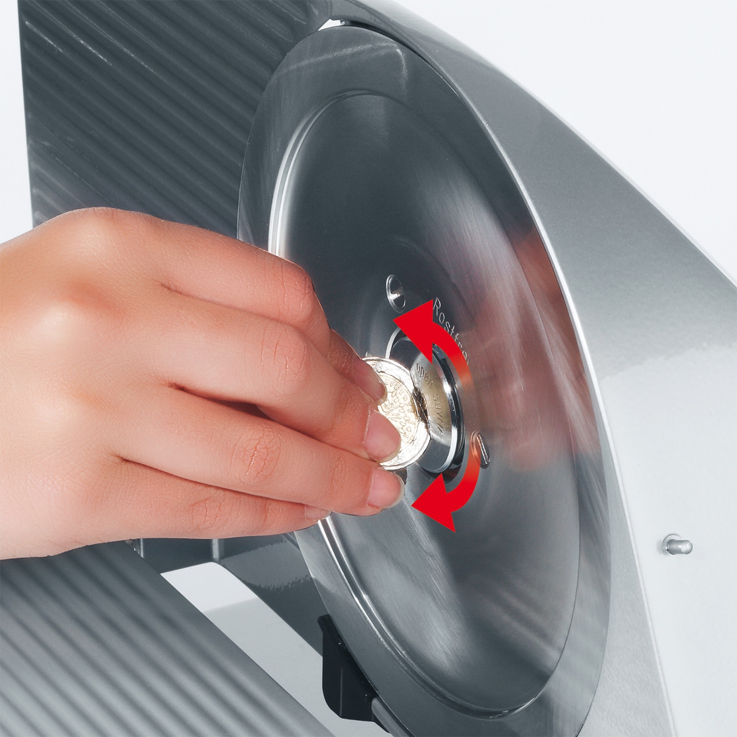 Hand turning coin in meat slicer to unlock blade, red arrows indicate direction.