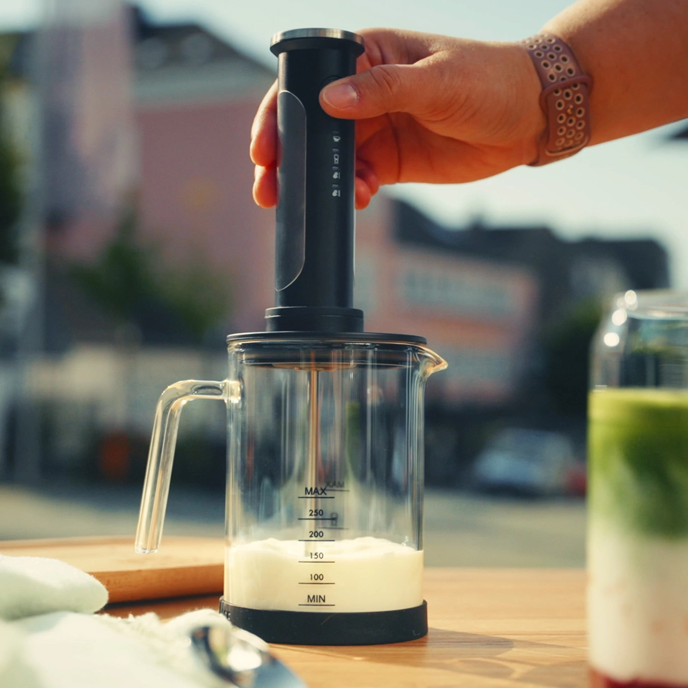 Eine Hand hält einen Milchaufschäumer über einem Glas mit Milch.