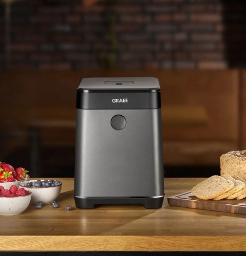 Graue Küchenmaschine mit Obst und Brot auf einem Holztisch
