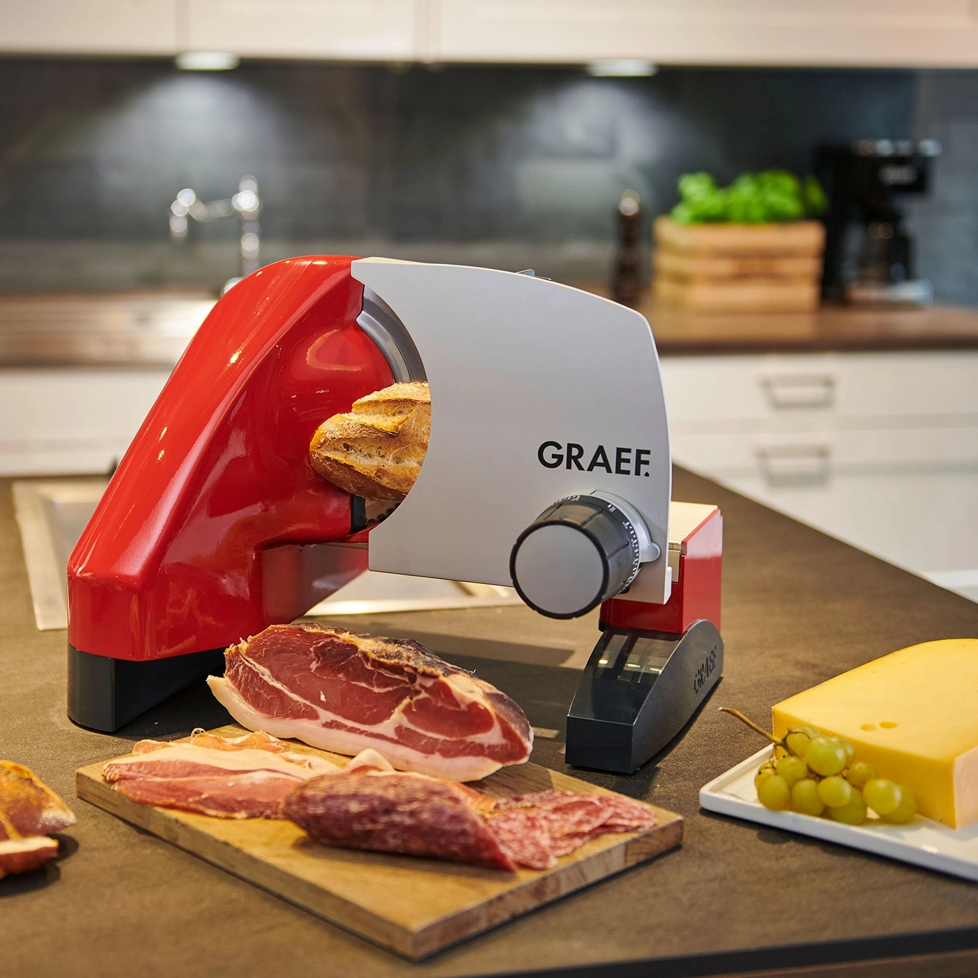 Roter Aufschnittschneider mit Brot, Wurst, Käse und Trauben auf dem Tisch.