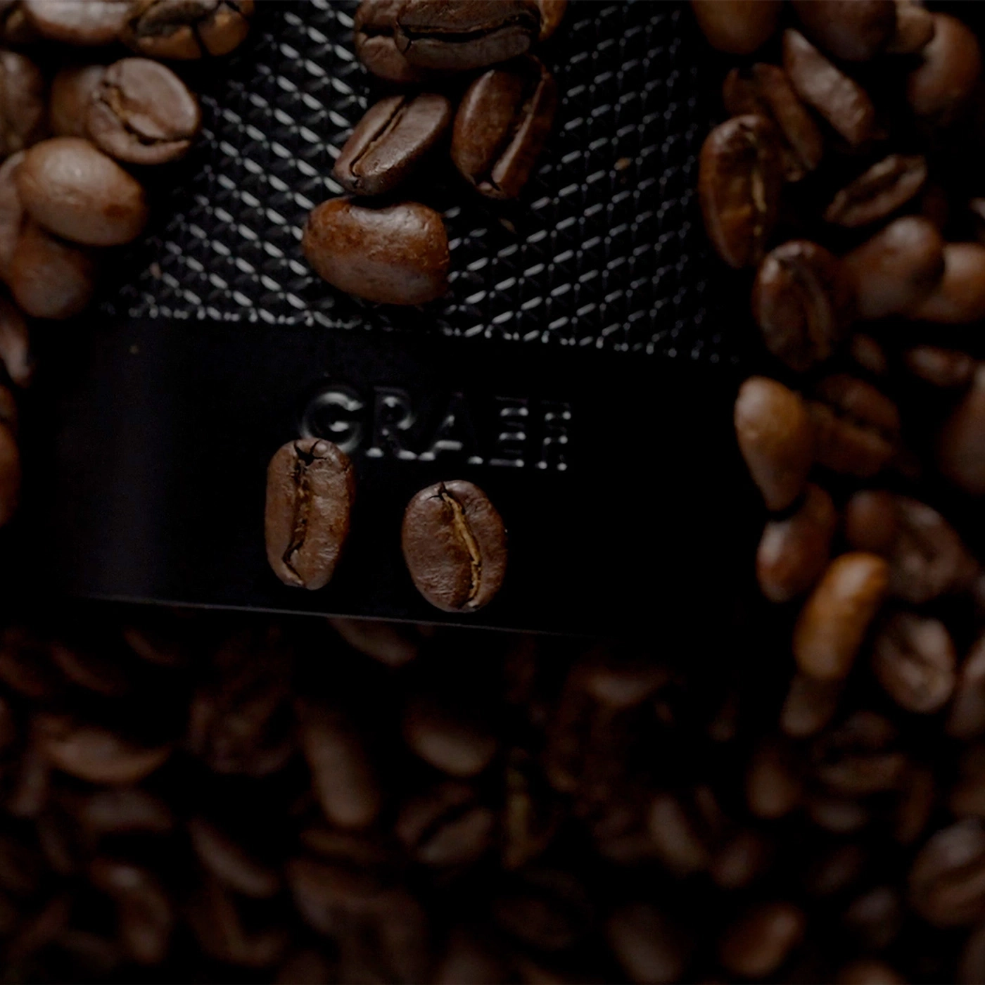 Roasted coffee beans surround a coffee grinder with the GRAEF logo.