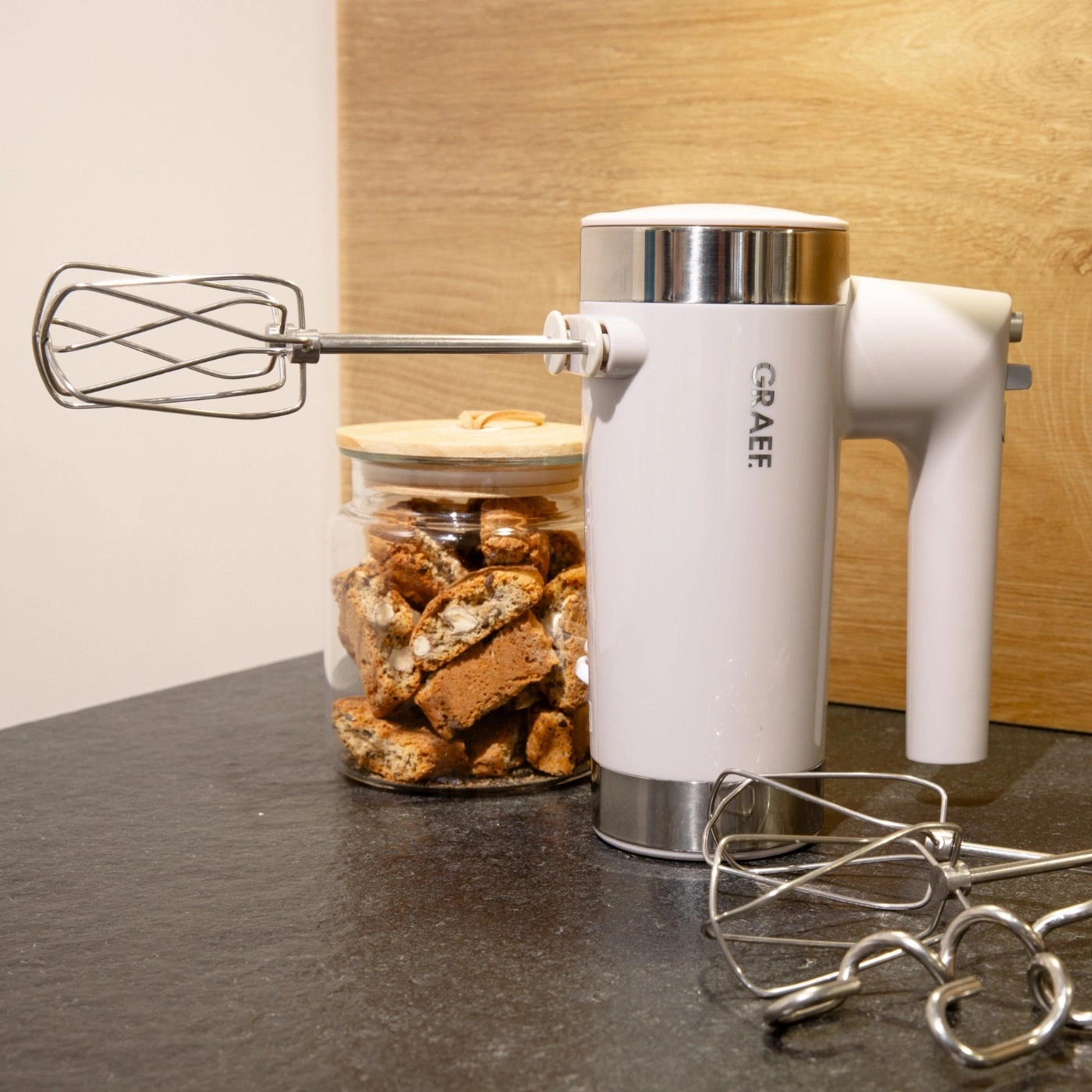 Hand mixer with accessories and cookies in a jar on a dark surface