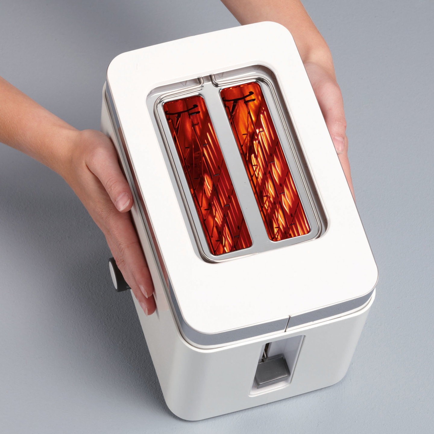 Weißer Toaster mit roten Heizdrähten, gehalten von Händen, auf grauem Hintergrund.