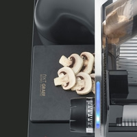 Mushrooms being sliced with a slicer machine on a black cutting board.