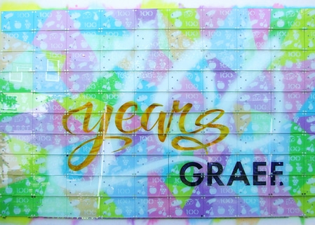 Buntes Wandbild mit "years" und "GRAEF", 100-Markierungen, Obst-Symbolen, farbenfroh.