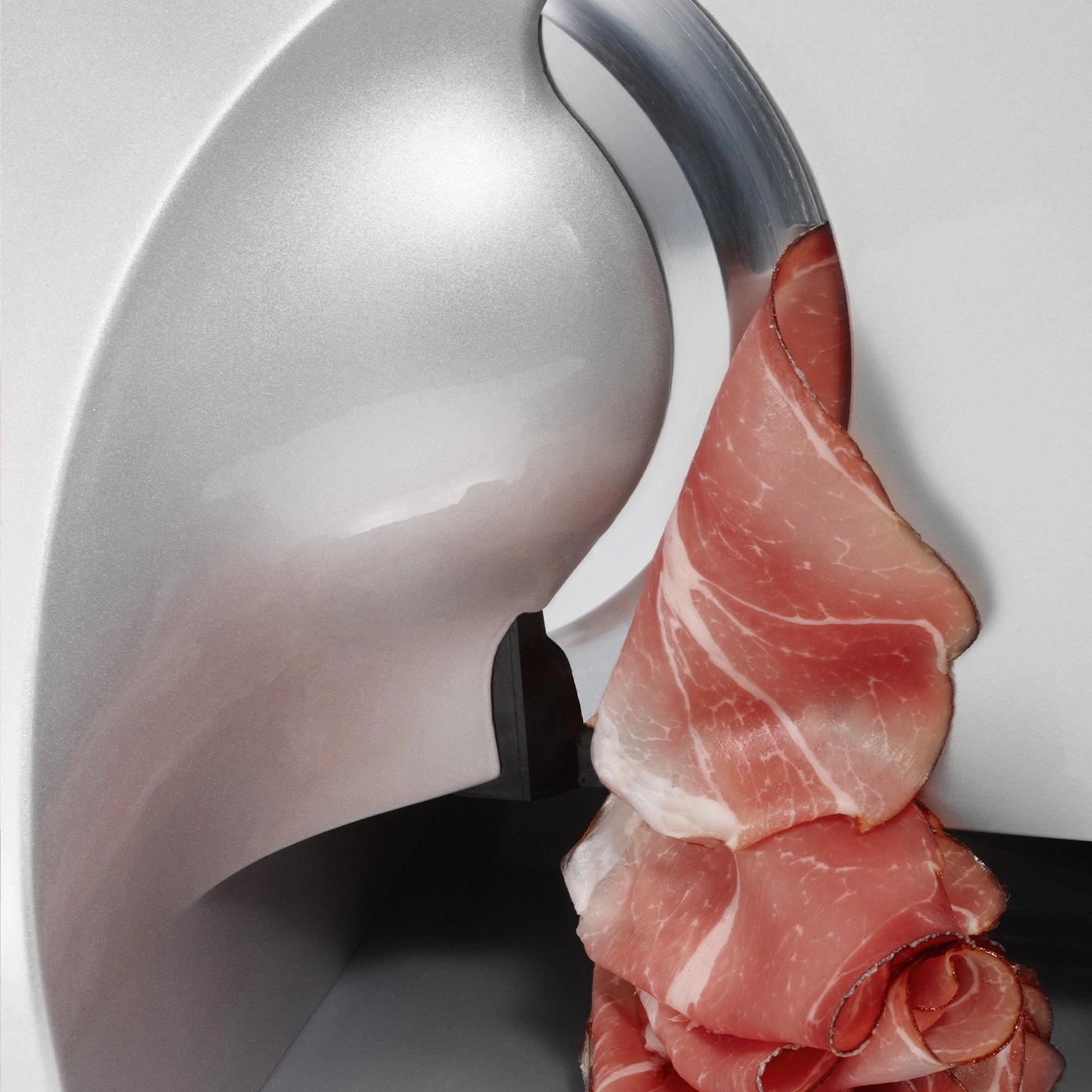 Close-up of a meat slicer slicing thin slices of ham, food preparation.