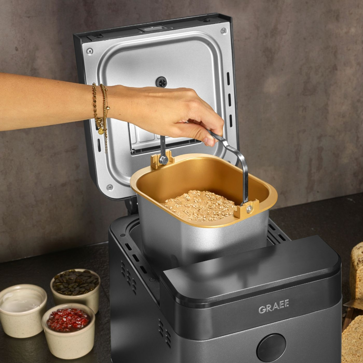Bread maker with ingredients and hand holding the container, close-up shot
