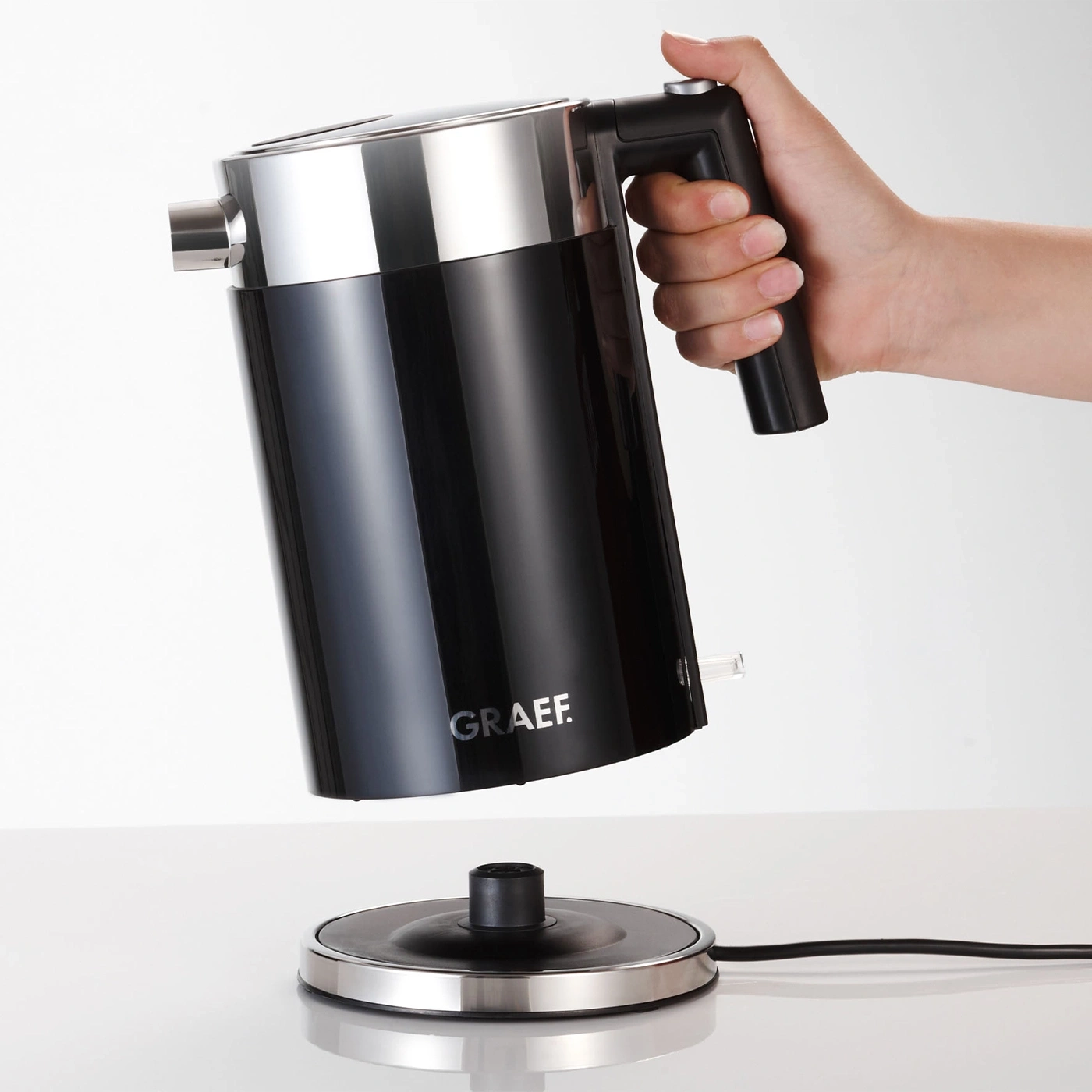 Black kettle with handle held by hand, on white background, with the brand name GRAEF.