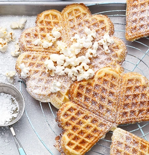 Herzförmige Waffeln mit Popcorn und Puderzucker auf einem Rost