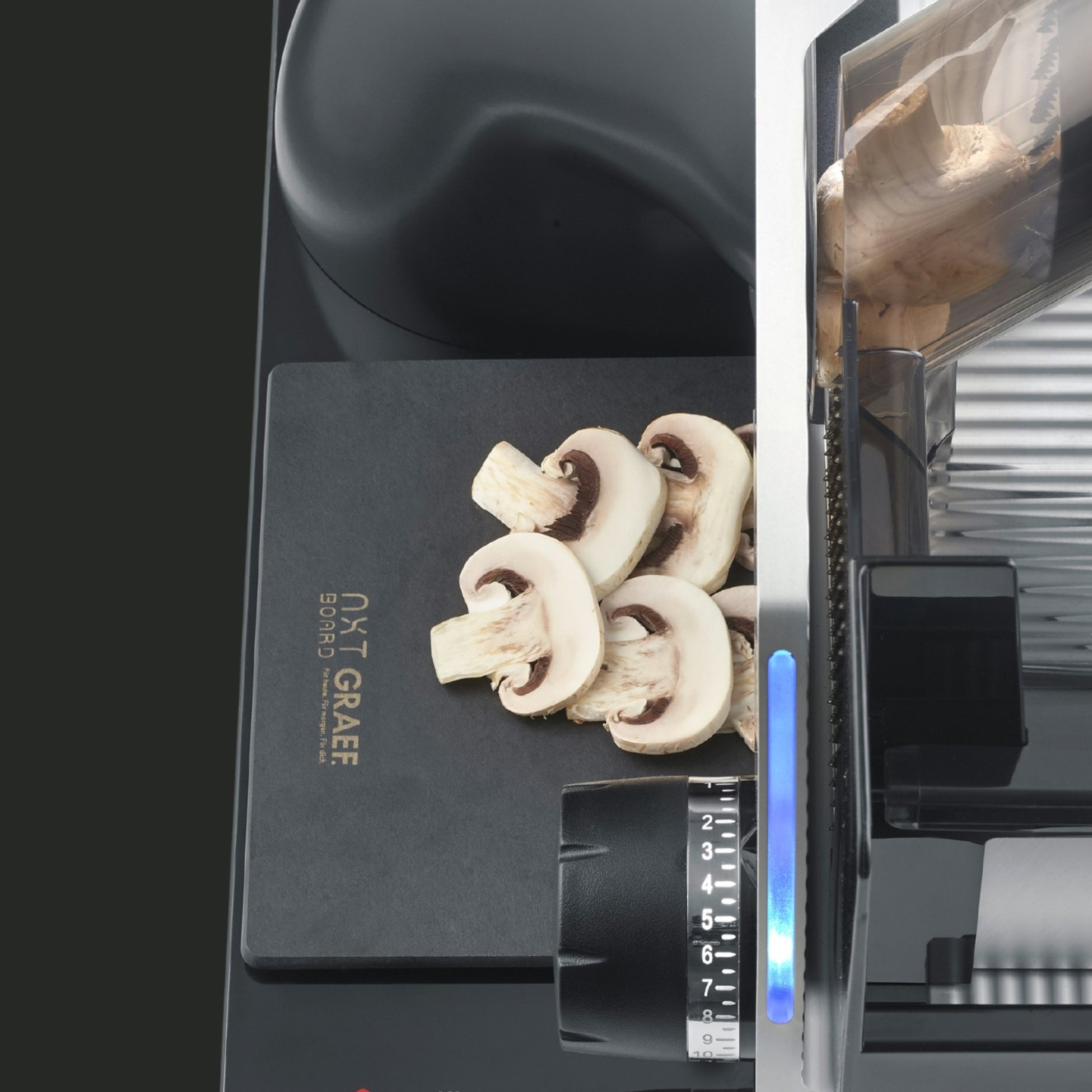 Pilze werden mit einer Schneidemaschine geschnitten. Auf einem schwarzen Brett.