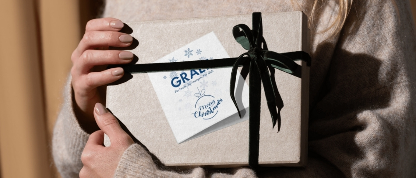 Person hält Geschenk mit Schleife und Karte mit Weihnachtsgrüßen