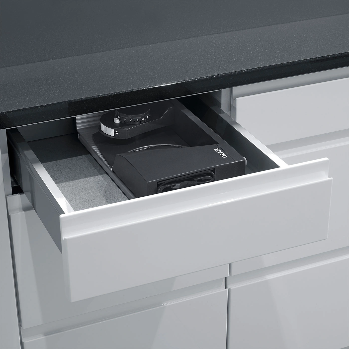 Drawer with coffee grinder, black countertop, kitchen cabinet, Graef logo visible.