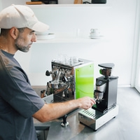 Mann bereitet Kaffee zu, mit Espressomaschine und Kaffeemühle.