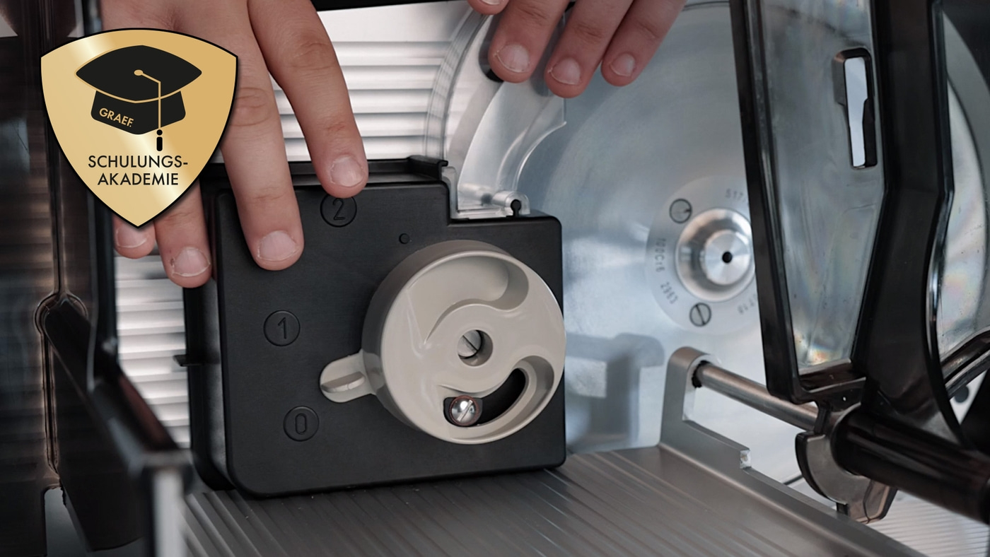 Nahaufnahme einer Schneidemaschine mit Händen und Logo der Schulungsakademie Graef.