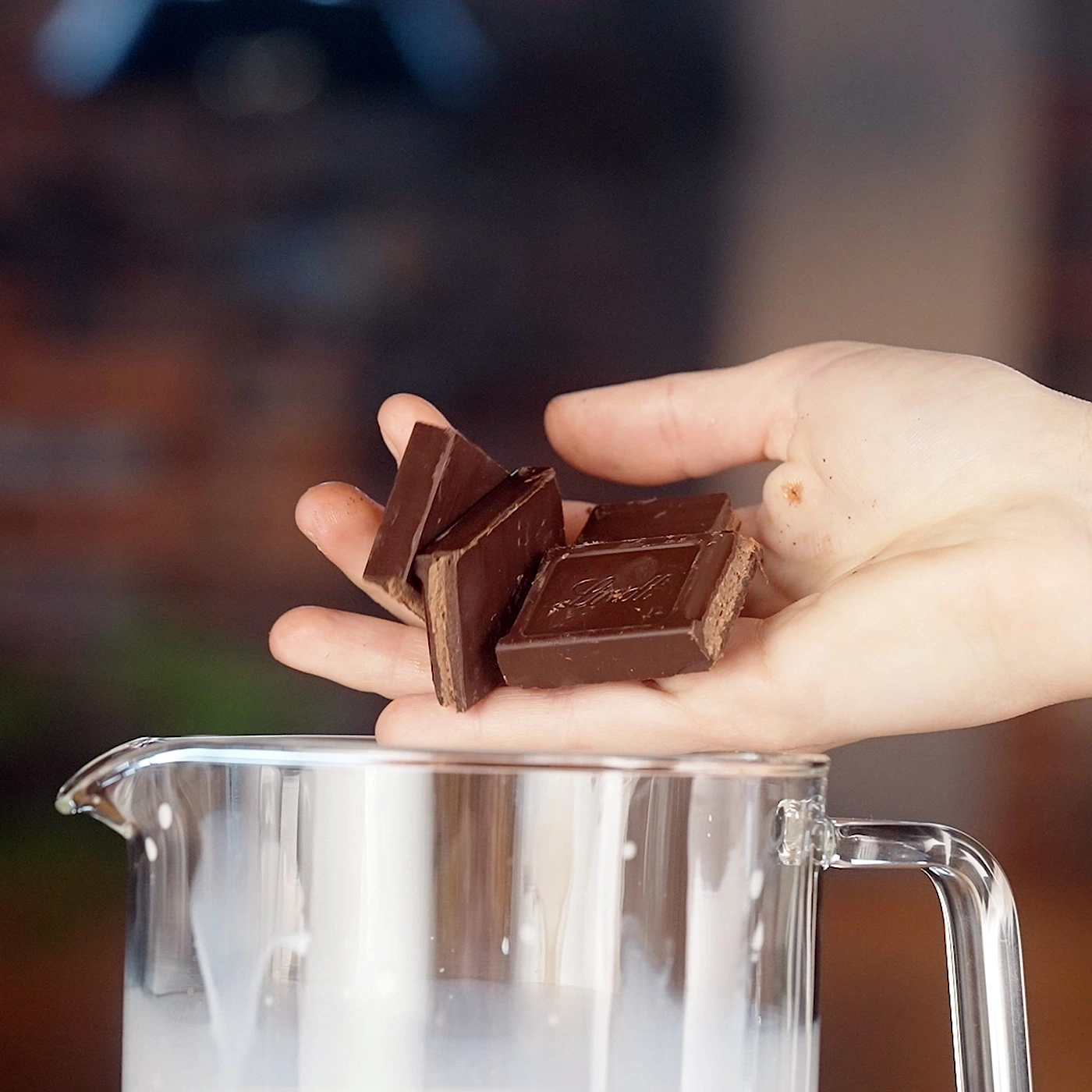 Hand hält Schokoladenstücke über einem Glas Milch.