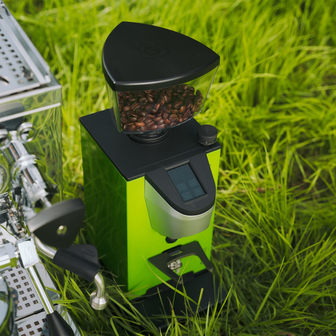 A green coffee grinder with beans on the grass.