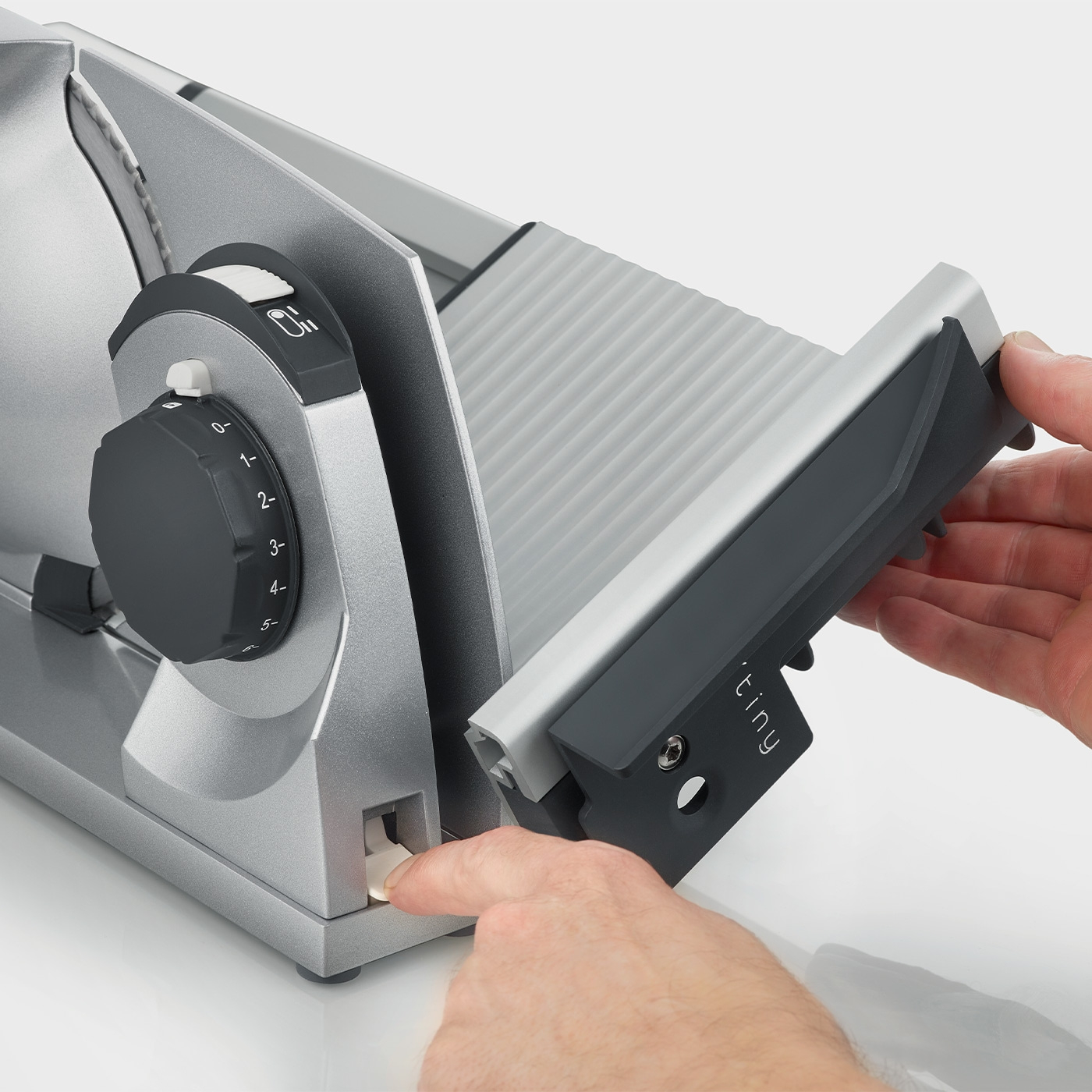 Close-up of a meat slicer being operated by two hands, detail view.