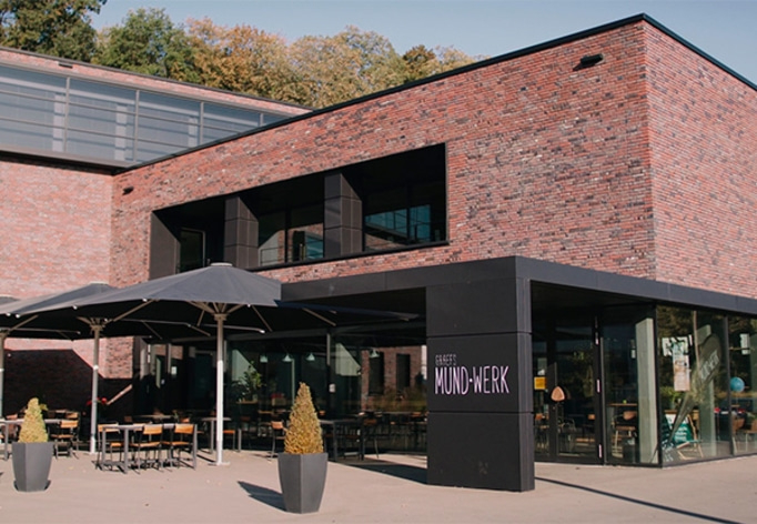 Gebäude mit Ziegelmauerwerk, Restaurant mit Außenbereich und Sonnenschirmen.