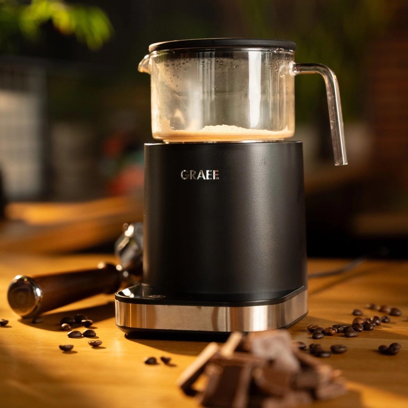 Kaffeemaschine mit Glasbehälter, Kaffeebohnen und Schokolade auf Holzoberfläche