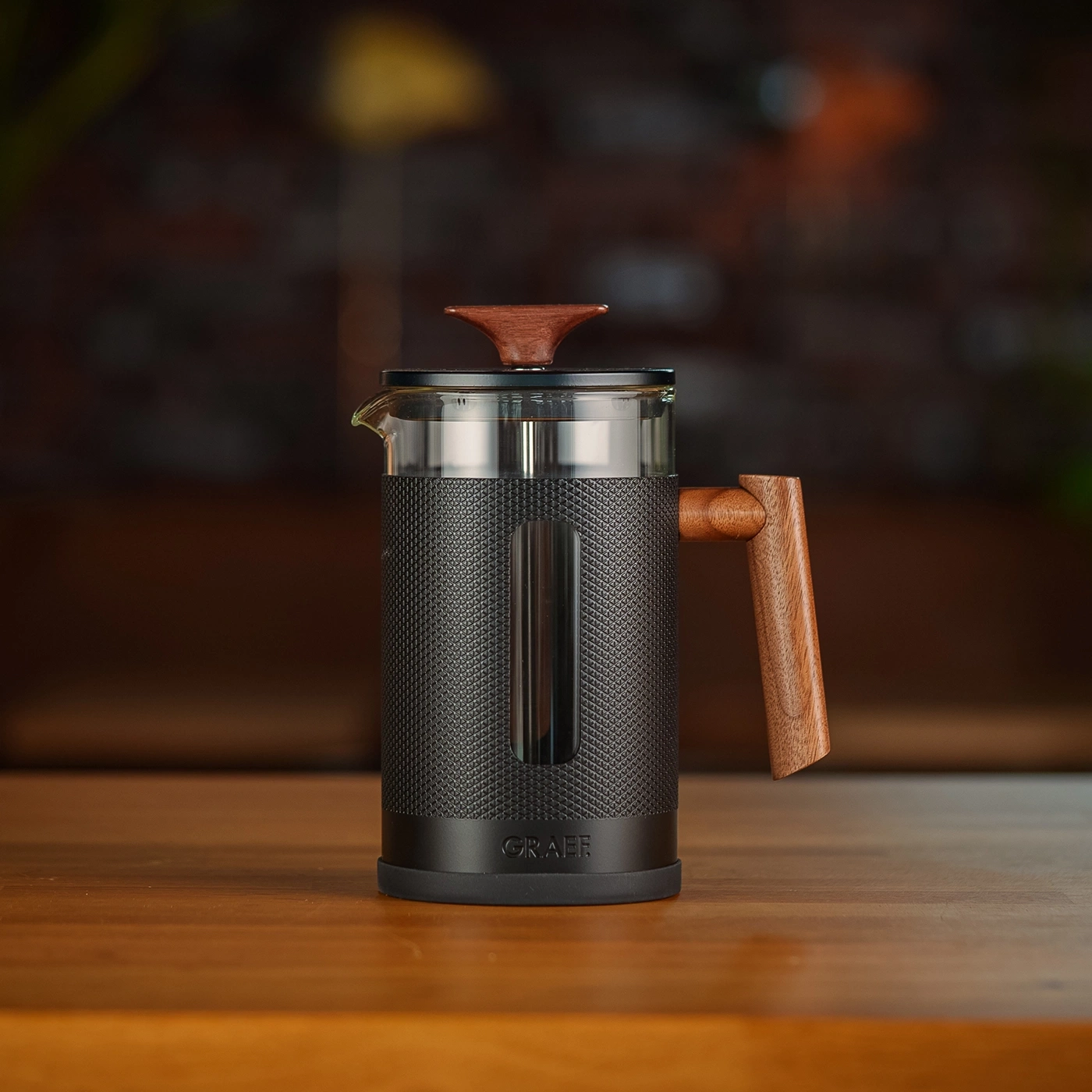 Coffee press with wooden handle and lid on a wooden table, GRAEF logo visible.