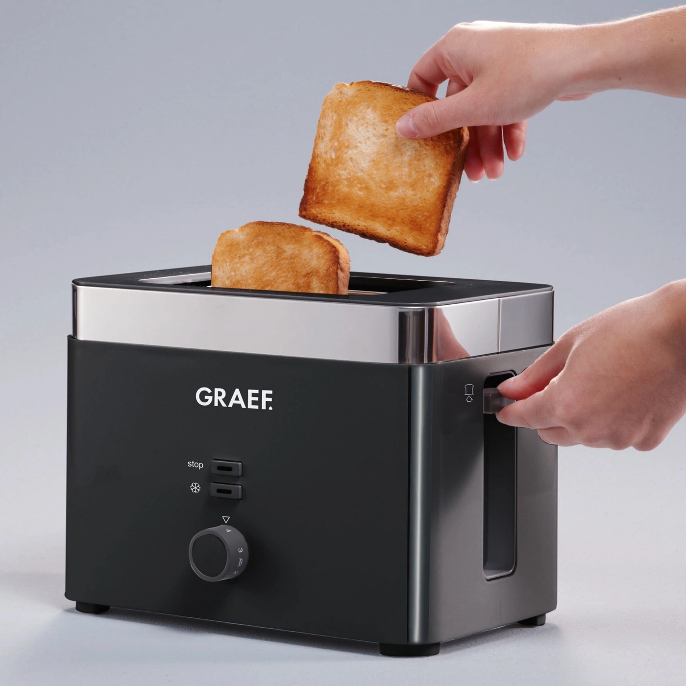 A toaster with two slices of toast being removed. A hand is operating the lever on the side.