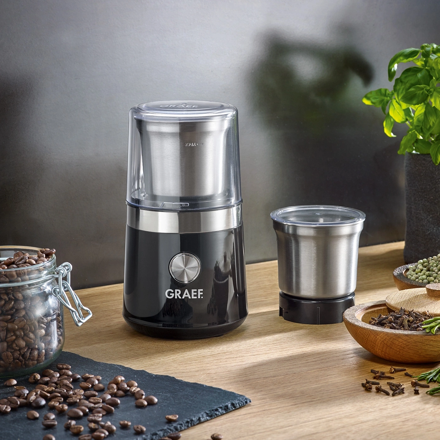 Coffee grinder with accessories and ingredients on wooden surface, close-up.