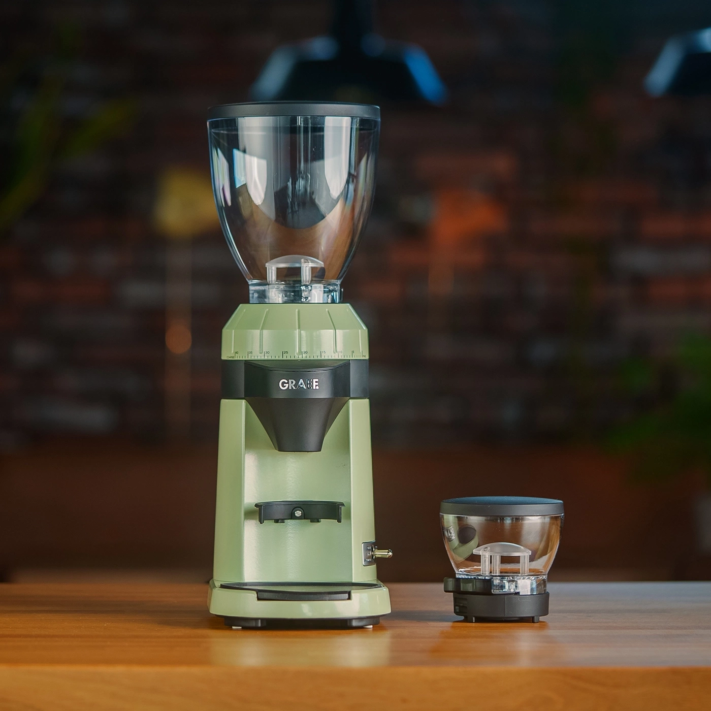 Eine hellgrüne elektrische Kaffeemühle von Graef mit Zubehör auf einem Holztisch.