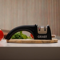 Schwarzer Messerschärfer mit Gemüse auf einem Holzbrett