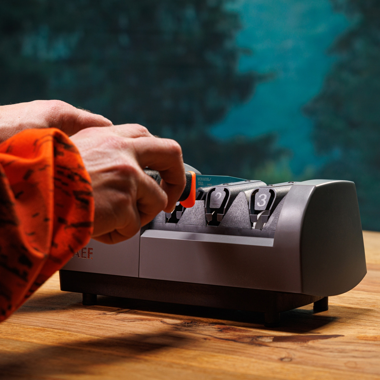 Person schärft Messer mit einem Messerschärfer auf einem Holztisch.