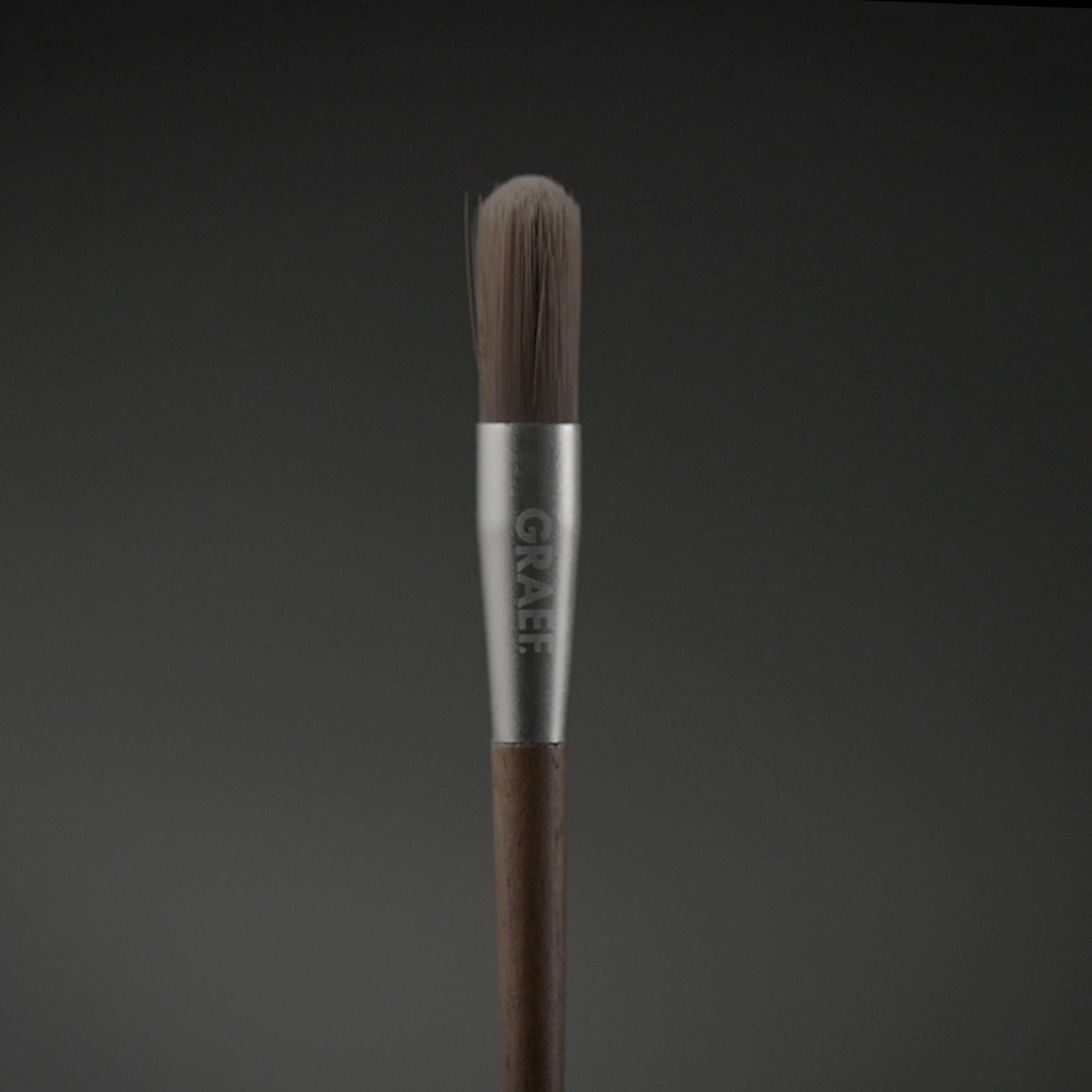 A makeup brush with a wooden handle and silver "GRAEF" imprint.
