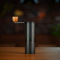 Close-up of a black coffee grinder with wooden handle on a wooden surface.