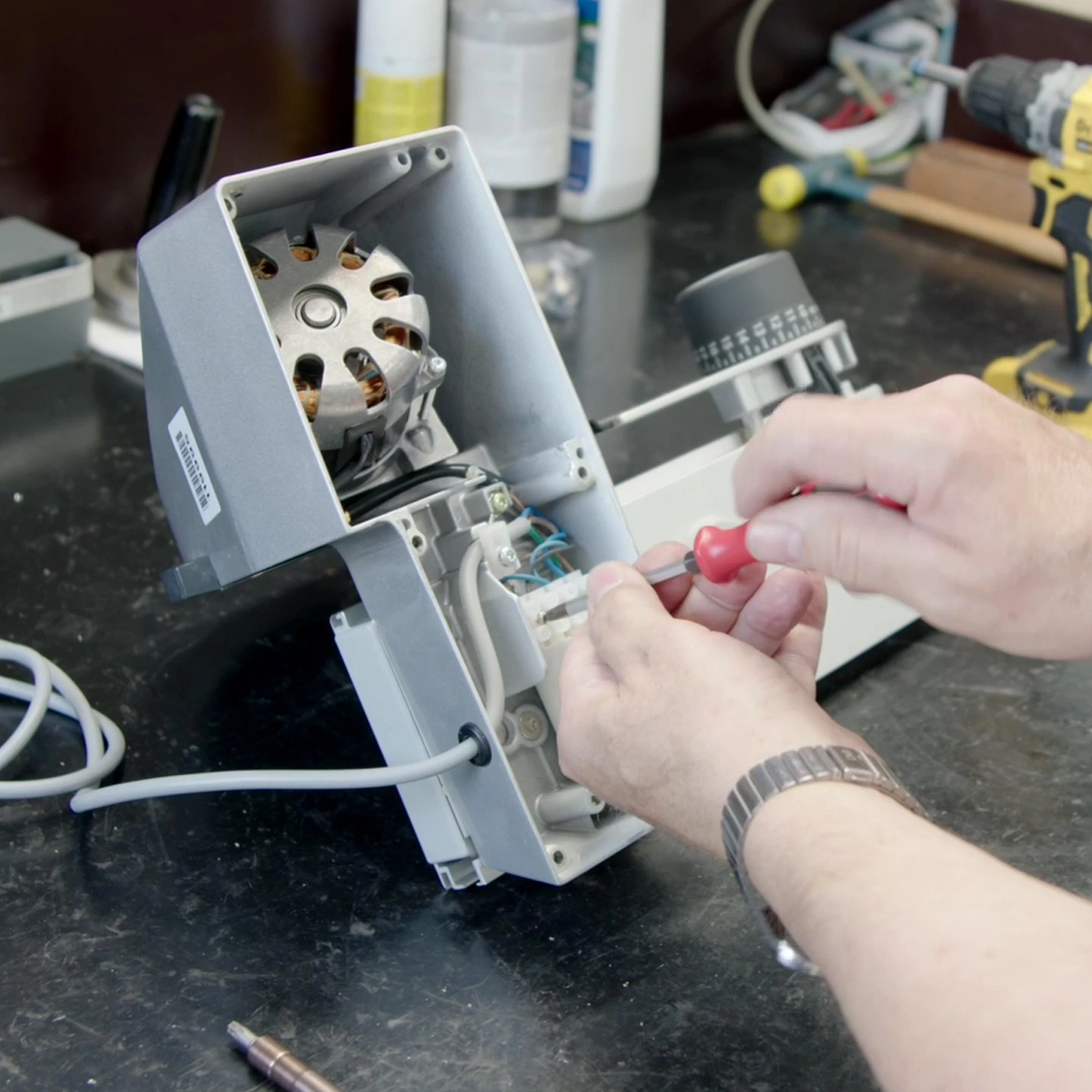 Person repairing device with screwdriver, close-up, workshop, technology