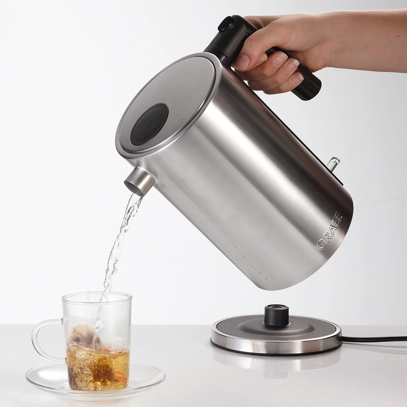 Eine Person gießt Wasser aus einem Wasserkocher in eine Teetasse.