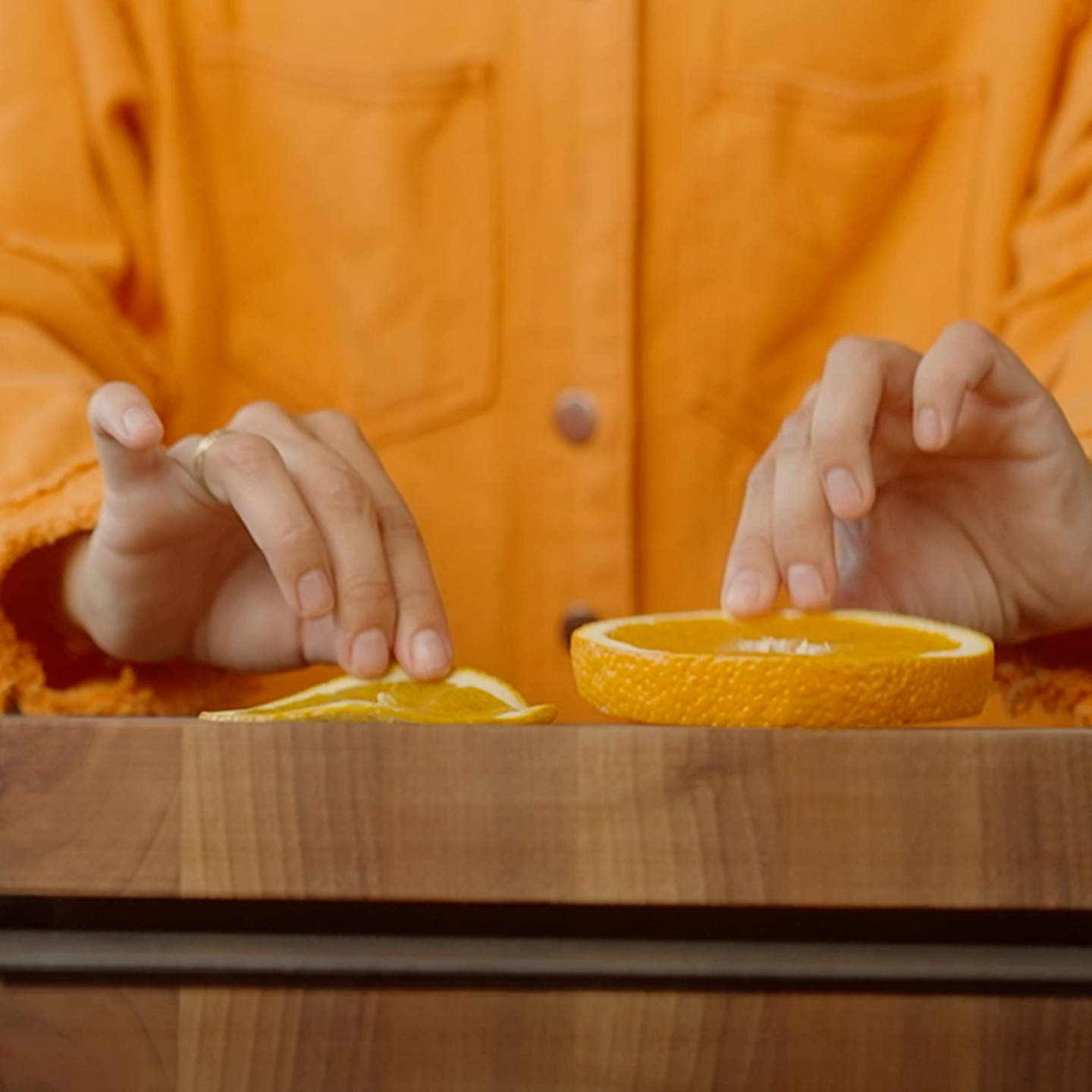 Person arrangiert Orangenstücke auf einem Holztisch, ein dünnes und ein dickes Stück.