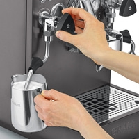 Person bereitet Milch auf einer Kaffeemaschine zu, um Kaffee zuzubereiten.