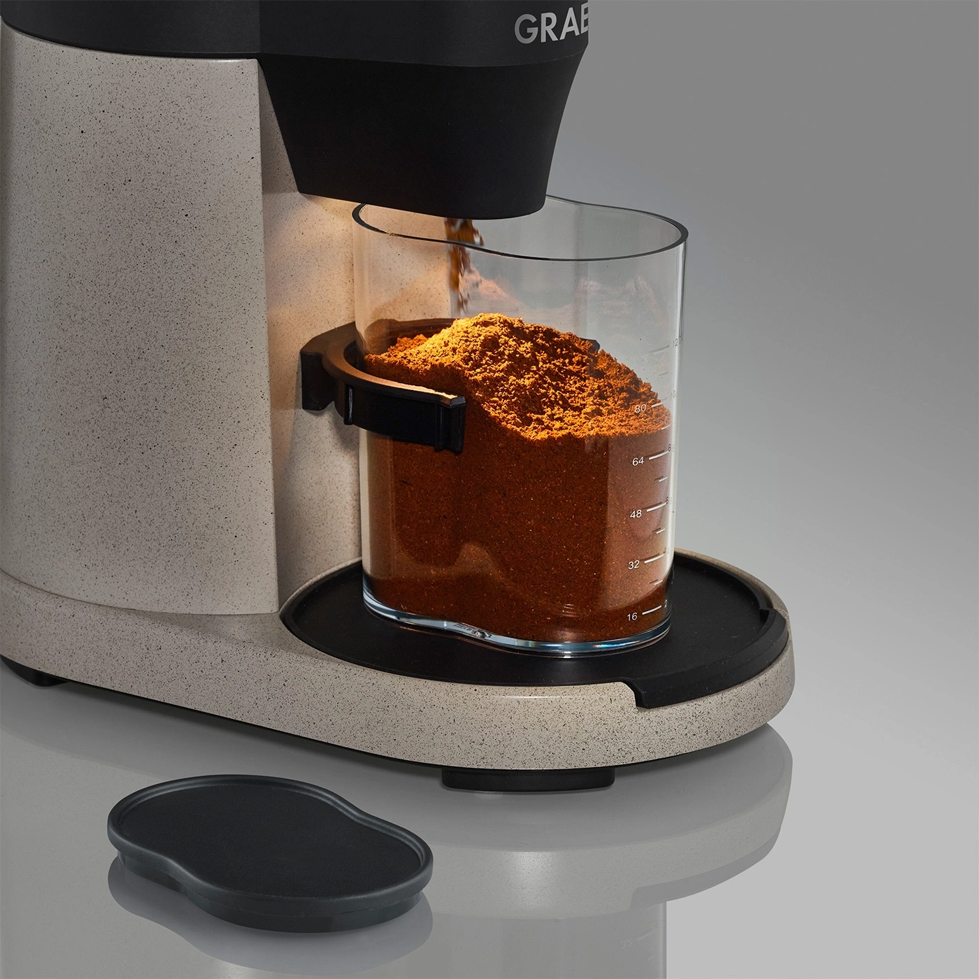 Kaffeemühle mit Glasbehälter, gefüllt mit Kaffeepulver, und schwarzem Deckel.