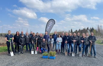Gruppe von Menschen mit Spaten vor Bäumen und blauem Himmel