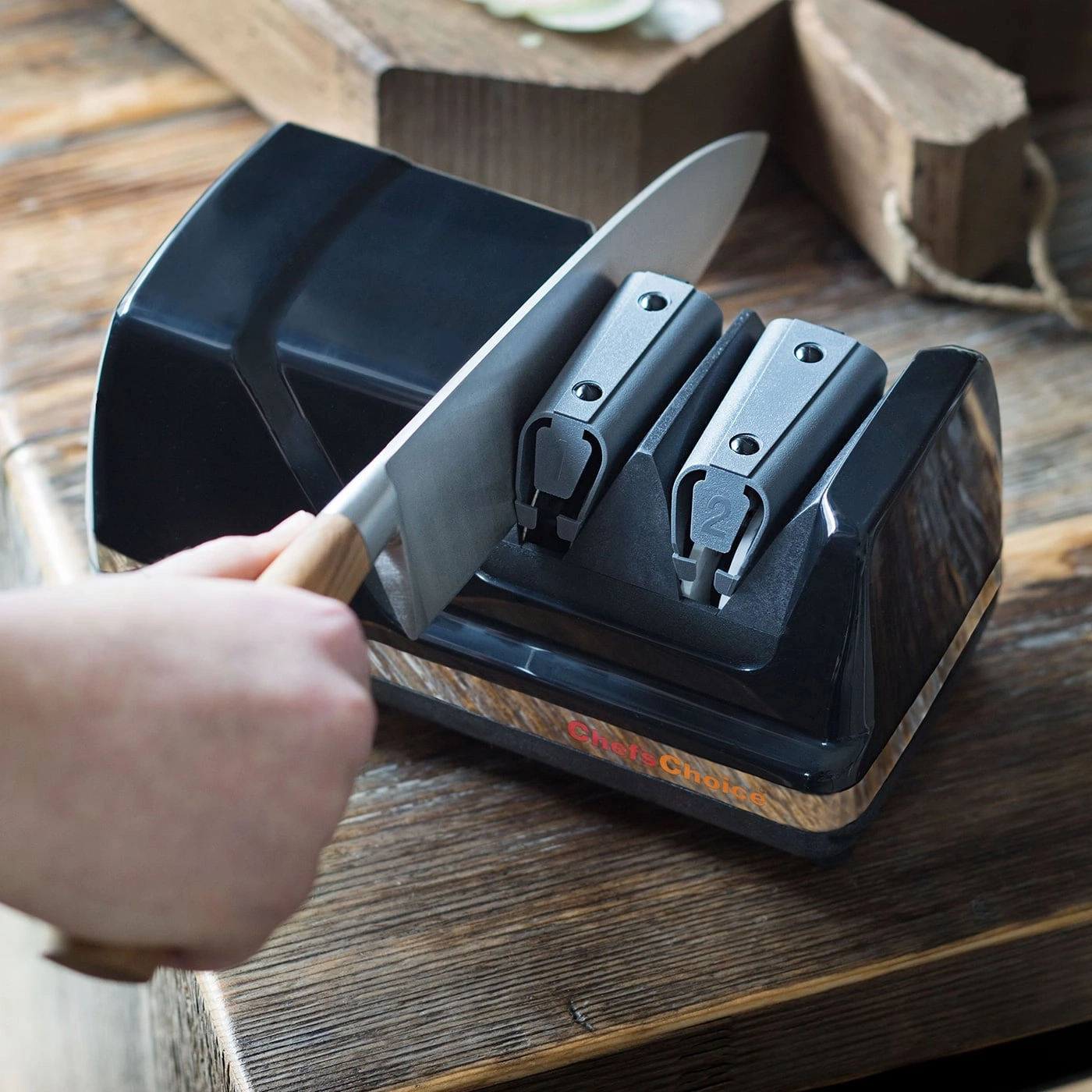 Knife being sharpened with a sharpener, close-up, wooden surface, Chef's Choice.