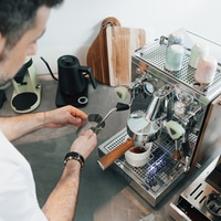 Mann bereitet Kaffee mit Espressomaschine zu, gießt Milch ein.
